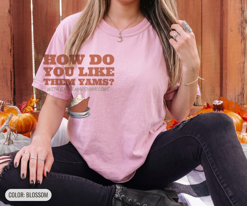 Blossom Comfort Colors t-shirt printed with the words How Do You Like Them Yams? With Extra Marshmallows and a drawing of a roasted yam sliced in half with melted marshmallow topping, worn by a woman