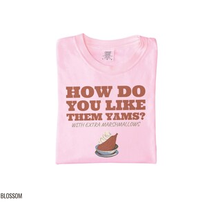 Blossom Comfort Colors t-shirt printed with the words How Do You Like Them Yams? With Extra Marshmallows and a drawing of a roasted yam sliced in half with melted marshmallow topping, folded flat lay
