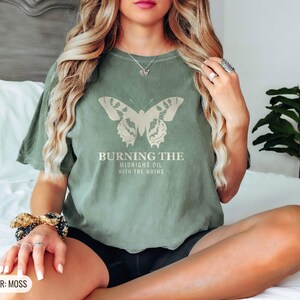Moss Comfort Colors t-shirt printed with the words Burning The Midnight Oil With The Moths and a drawing of a cecropia moth with feathery antennae, worn by a woman
