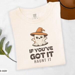 Ivory Comfort Colors t-shirt printed with the words If You'Ve Got It Haunt It and a drawing of a cute retro cartoon ghost wearing a witch hat, folded flat lay