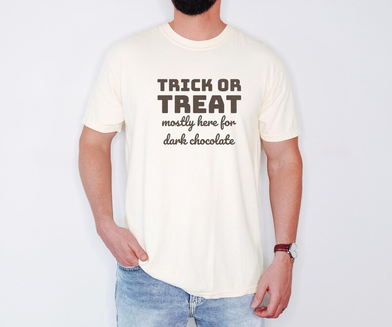 Ivory Comfort Colors t-shirt printed with the words Trick Or Treat Mostly Here For Dark Chocolate, worn by a man