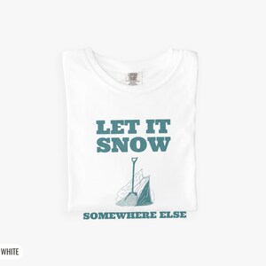 White Comfort Colors t-shirt printed with the words Let It Snow Somewhere Else and a drawing of a metal snow shovel propped beside an empty bag of rock salt, folded flat lay
