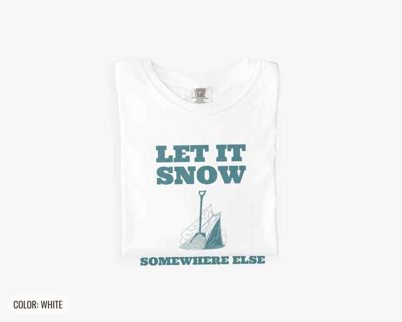 White Comfort Colors t-shirt printed with the words Let It Snow Somewhere Else and a drawing of a metal snow shovel propped beside an empty bag of rock salt, folded flat lay