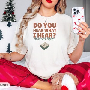 Ivory Comfort Colors t-shirt printed with the words Do You Hear What I Hear? Just Call Lights and a drawing of a rectangular electronic medical pager with a small holly sprig beside it, worn by a woman