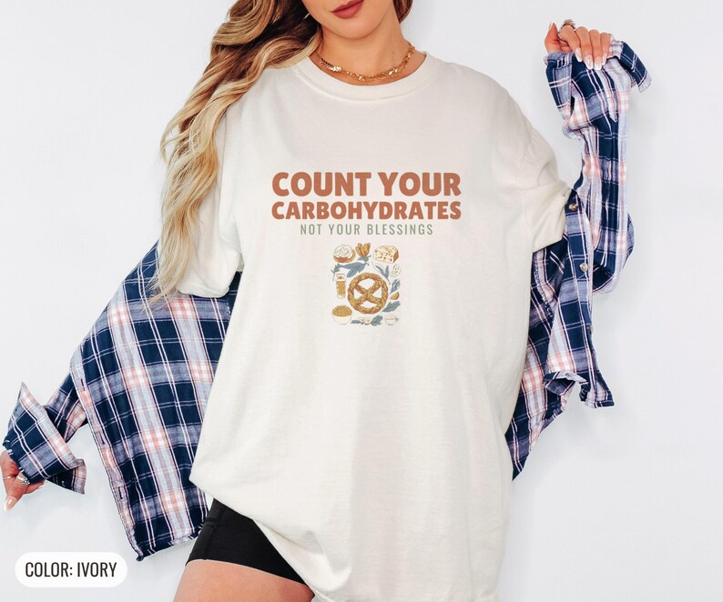 Ivory Comfort Colors t-shirt printed with the words Count Your Carbohydrates Not Your Blessings and a drawing of a golden-brown braided pretzel with coarse salt grains, worn by a woman