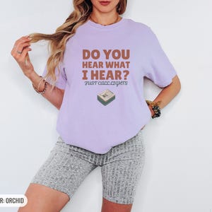 Orchid Comfort Colors t-shirt printed with the words Do You Hear What I Hear? Just Call Lights and a drawing of a rectangular electronic medical pager with a small holly sprig beside it, worn by a woman