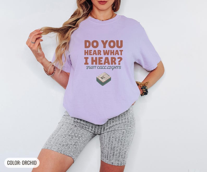 Orchid Comfort Colors t-shirt printed with the words Do You Hear What I Hear? Just Call Lights and a drawing of a rectangular electronic medical pager with a small holly sprig beside it, worn by a woman