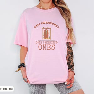 Blossom Comfort Colors t-shirt printed with the words Got Sweaters? Only Oversized Ones and a drawing of a knitted wool cardigan hanging from a simple wooden clothes hanger, worn by a woman