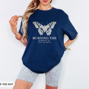 True Navy Comfort Colors t-shirt printed with the words Burning The Midnight Oil With The Moths and a drawing of a cecropia moth with feathery antennae, worn by a woman