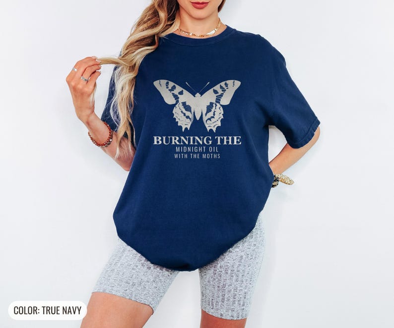 True Navy Comfort Colors t-shirt printed with the words Burning The Midnight Oil With The Moths and a drawing of a cecropia moth with feathery antennae, worn by a woman