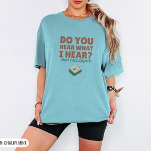 Chalky Mint Comfort Colors t-shirt printed with the words Do You Hear What I Hear? Just Call Lights and a drawing of a rectangular electronic medical pager with a small holly sprig beside it, worn by a woman