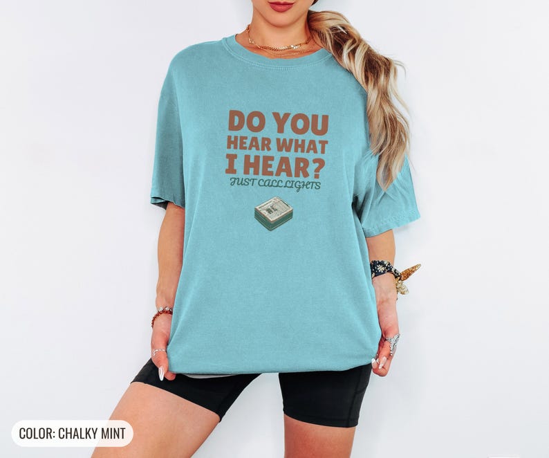 Chalky Mint Comfort Colors t-shirt printed with the words Do You Hear What I Hear? Just Call Lights and a drawing of a rectangular electronic medical pager with a small holly sprig beside it, worn by a woman