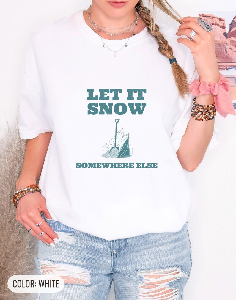 White Comfort Colors t-shirt printed with the words Let It Snow Somewhere Else and a drawing of a metal snow shovel propped beside an empty bag of rock salt, worn by a woman