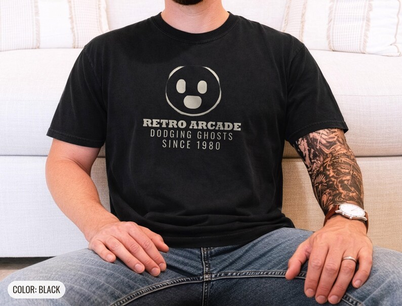 Black Comfort Colors t-shirt printed with the words Retro Arcade Dodging Ghosts Since 1980 and a drawing of a maze with a Pac-Man character, worn by a man
