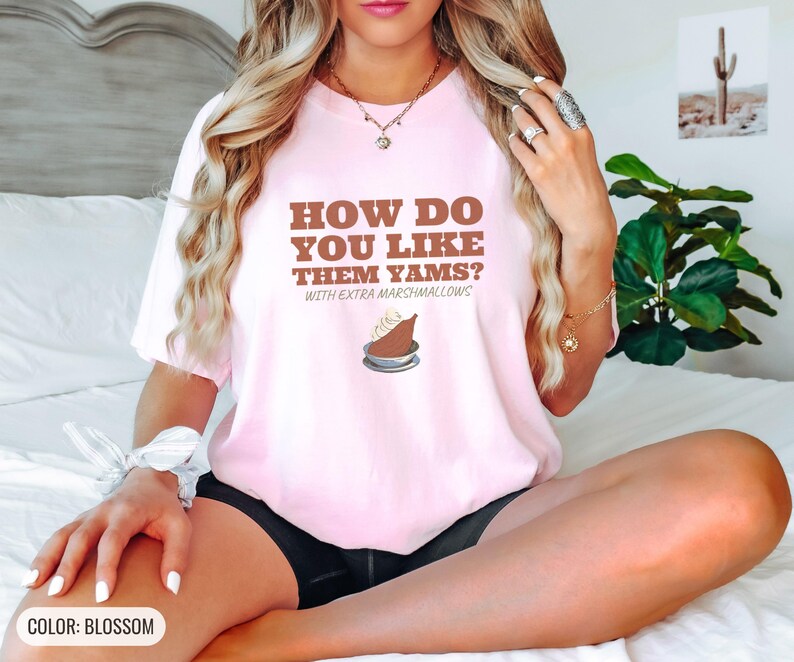 Blossom Comfort Colors t-shirt printed with the words How Do You Like Them Yams? With Extra Marshmallows and a drawing of a roasted yam sliced in half with melted marshmallow topping, worn by a woman