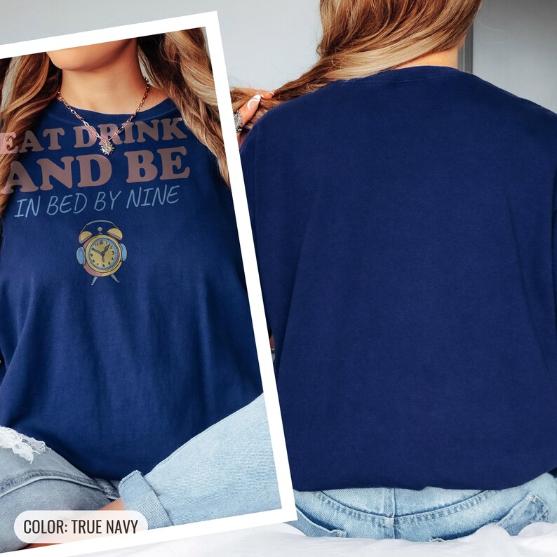 True Navy Comfort Colors t-shirt printed with the words Eat Drink And Be In Bed By Nine and a drawing of a retro brass wind-up alarm clock with its bells wrapped in fuzzy winter earmuffs, worn by a woman