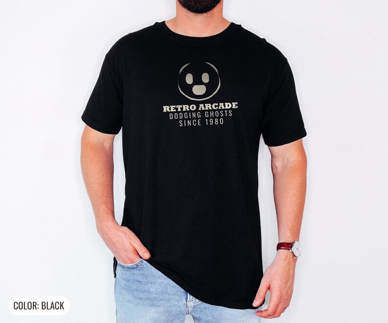 Black Comfort Colors t-shirt printed with the words Retro Arcade Dodging Ghosts Since 1980 and a drawing of a maze with a Pac-Man character, worn by a man