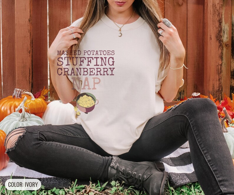 Ivory Comfort Colors t-shirt printed with the words Mashed Potatoes Stuffing Cranberry Nap and a drawing of a heavy enamel-coated cast iron Dutch oven filled with creamy mashed potatoes, steam lines, worn by a woman