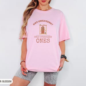 Blossom Comfort Colors t-shirt printed with the words Got Sweaters? Only Oversized Ones and a drawing of a knitted wool cardigan hanging from a simple wooden clothes hanger, worn by a woman