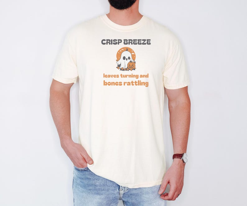 Ivory Comfort Colors t-shirt printed with the words Crisp Breeze Leaves Turning And Bones Rattling and a drawing of a large cute smiling ghost beside a carved jack-o-lantern, worn by a man