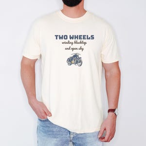 Ivory Comfort Colors t-shirt printed with the words Two Wheels Winding Blacktop And Open Sky and a drawing of a classic cruiser motorcycle in side profile, worn by a man