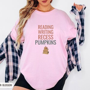 Blossom Comfort Colors t-shirt printed with the words Reading Writing Recess Pumpkins and a drawing of a stack of three vintage schoolbooks with a small orange pumpkin sitting on top, worn by a woman