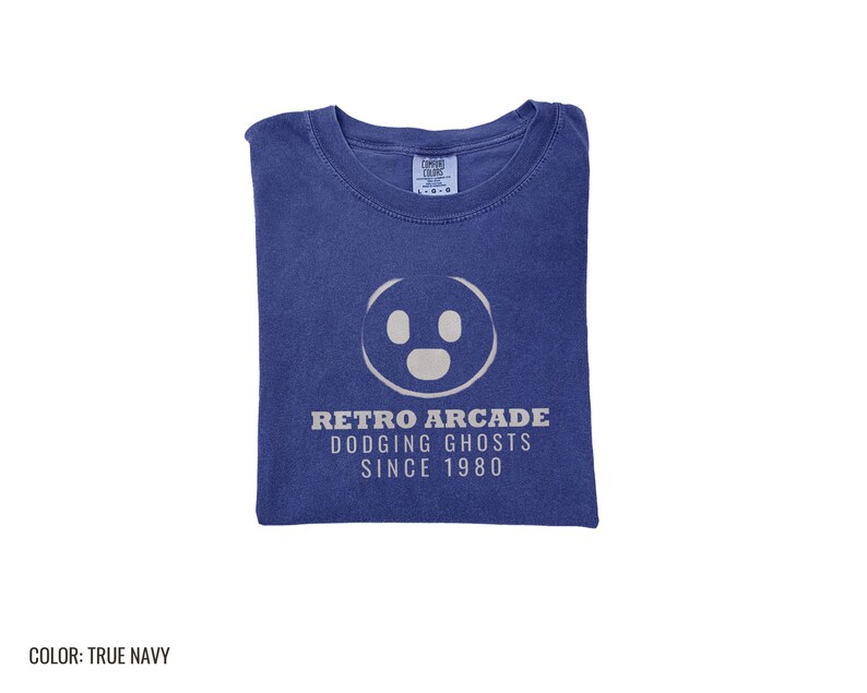 True Navy Comfort Colors t-shirt printed with the words Retro Arcade Dodging Ghosts Since 1980 and a drawing of a maze with a Pac-Man character, folded flat lay