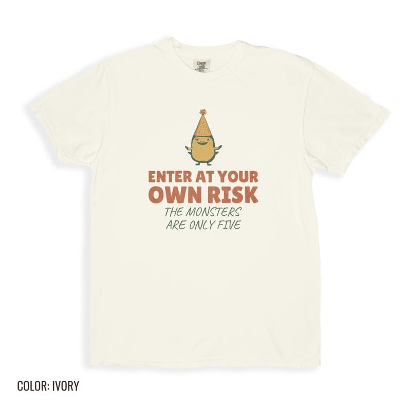 Ivory Comfort Colors t-shirt printed with the words Enter At Your Own Risk The Monsters Are Only Five and a drawing of a cute, smiling little green monster wearing a tiny paper party hat and holding a crayon, folded flat lay