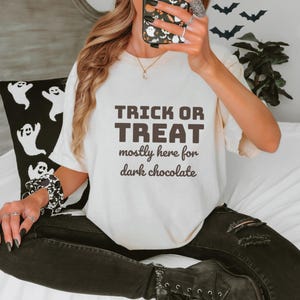 Ivory Comfort Colors t-shirt printed with the words Trick Or Treat Mostly Here For Dark Chocolate, worn by a woman
