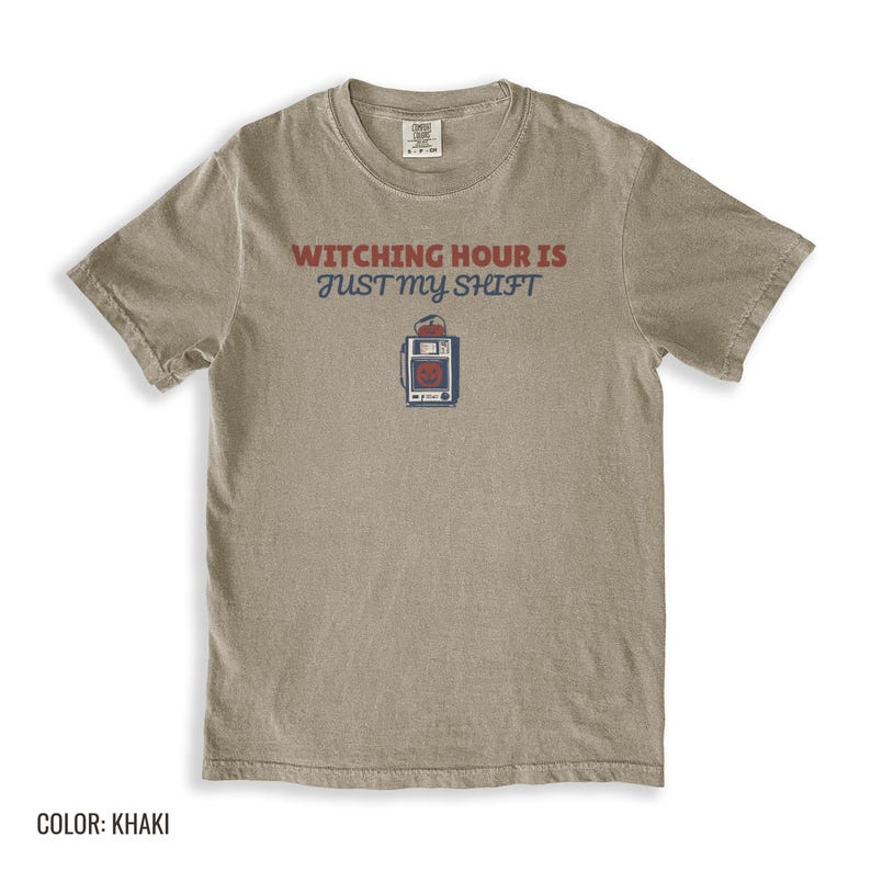 Khaki Comfort Colors t-shirt printed with the words Witching Hour Is Just My Shift and a drawing of a retro medical defibrillator machine decorated with a spooky jack-o-lantern face on its m, folded flat lay