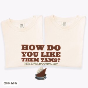 Ivory Comfort Colors t-shirt printed with the words How Do You Like Them Yams? With Extra Marshmallows and a drawing of a roasted yam sliced in half with melted marshmallow topping, two matching shirts