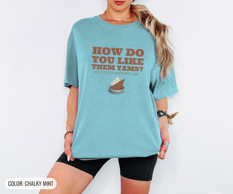 Chalky Mint Comfort Colors t-shirt printed with the words How Do You Like Them Yams? With Extra Marshmallows and a drawing of a roasted yam sliced in half with melted marshmallow topping, worn by a woman
