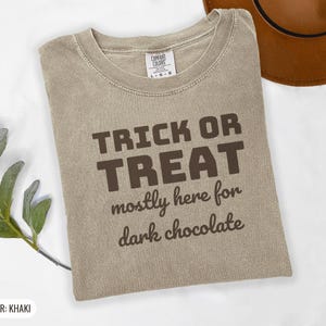 Khaki Comfort Colors t-shirt printed with the words Trick Or Treat Mostly Here For Dark Chocolate, folded flat lay