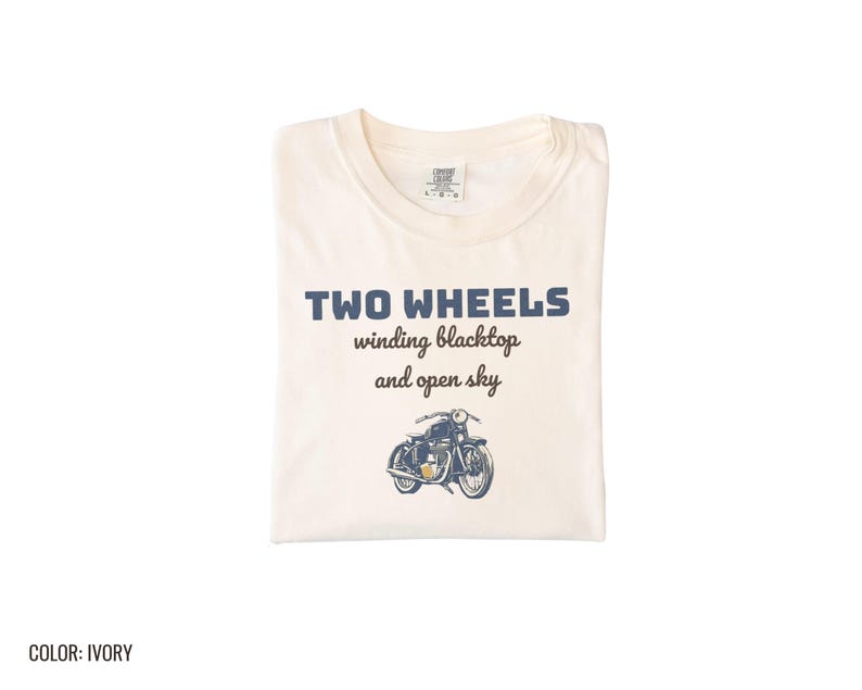 Ivory Comfort Colors t-shirt printed with the words Two Wheels Winding Blacktop And Open Sky and a drawing of a classic cruiser motorcycle in side profile, folded flat lay