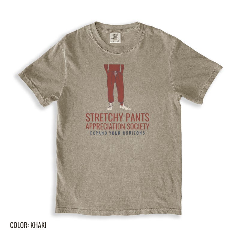 Khaki Comfort Colors t-shirt printed with the words Stretchy Pants Appreciation Society Expand Your Horizons and a drawing of a pair of classic grey sweatpants with a visible drawstring, folded flat lay