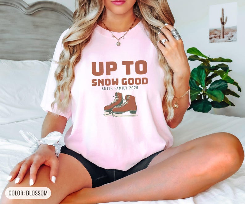 Blossom Comfort Colors t-shirt printed with the words Up To Snow Good Smith Family 2026 and a drawing of a vintage metal clamp-on ice skate with red laces, worn by a woman