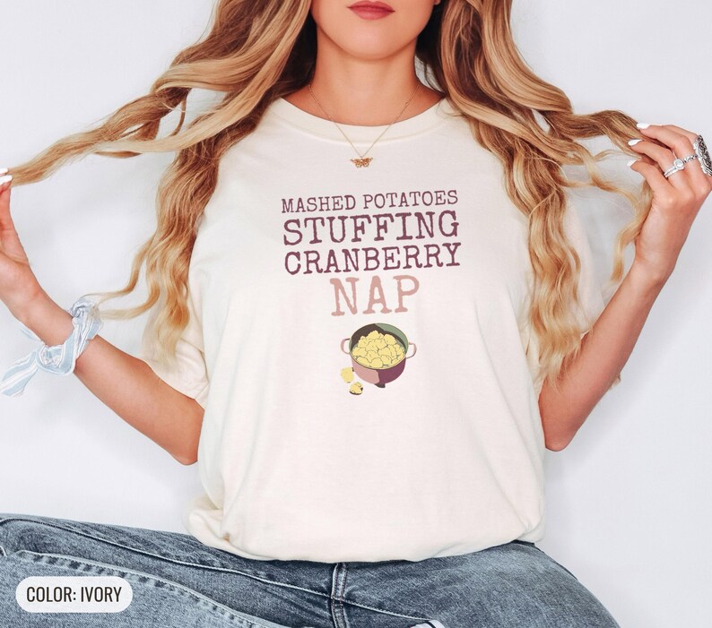 Ivory Comfort Colors t-shirt printed with the words Mashed Potatoes Stuffing Cranberry Nap and a drawing of a heavy enamel-coated cast iron Dutch oven filled with creamy mashed potatoes, steam lines, worn by a woman