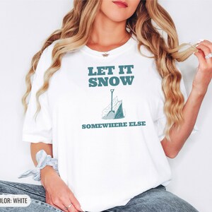 White Comfort Colors t-shirt printed with the words Let It Snow Somewhere Else and a drawing of a metal snow shovel propped beside an empty bag of rock salt, worn by a woman