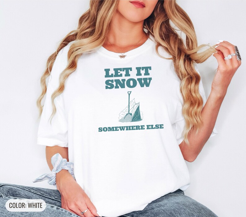 White Comfort Colors t-shirt printed with the words Let It Snow Somewhere Else and a drawing of a metal snow shovel propped beside an empty bag of rock salt, worn by a woman