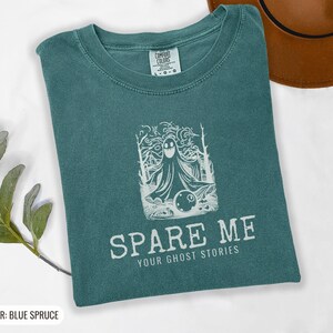 Blue Spruce Comfort Colors t-shirt printed with the words Spare Me Your Ghost Stories and a drawing of a friendly sheet ghost rolling a bowling ball towards a set of bowling pins, folded flat lay
