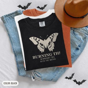 Black Comfort Colors t-shirt printed with the words Burning The Midnight Oil With The Moths and a drawing of a cecropia moth with feathery antennae, worn by a woman