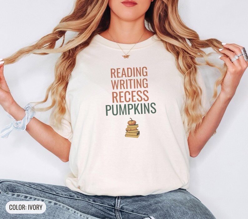 Ivory Comfort Colors t-shirt printed with the words Reading Writing Recess Pumpkins and a drawing of a stack of three vintage schoolbooks with a small orange pumpkin sitting on top, worn by a woman