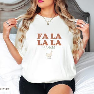 Ivory Comfort Colors t-shirt printed with the words Fa La La La Llama and a drawing of a fluffy llama, worn by a woman