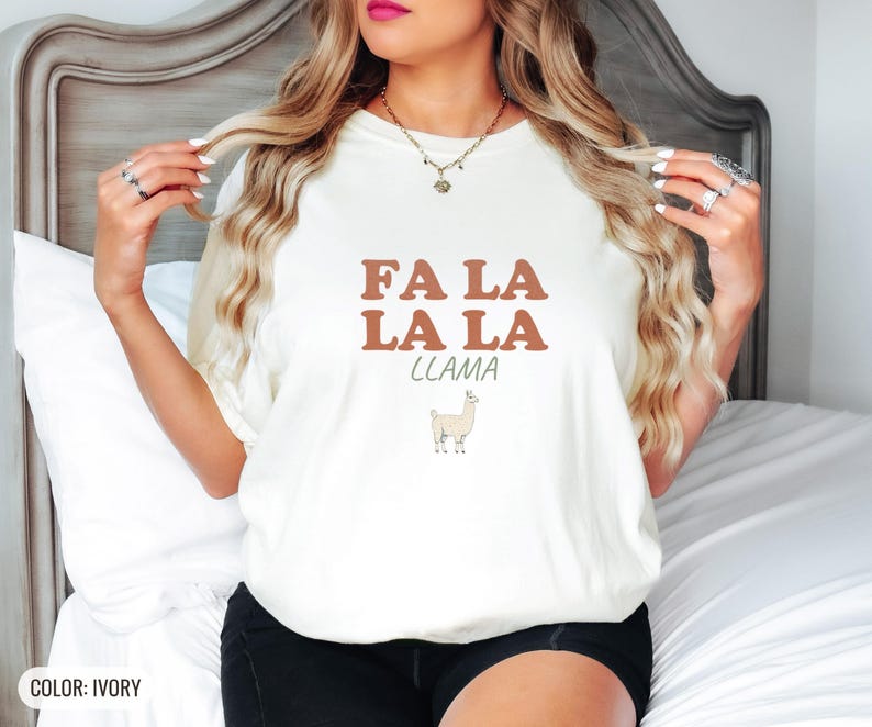 Ivory Comfort Colors t-shirt printed with the words Fa La La La Llama and a drawing of a fluffy llama, worn by a woman