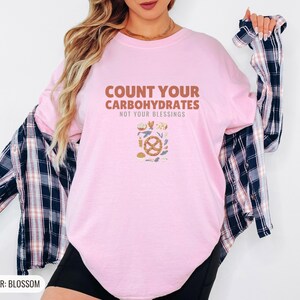 Blossom Comfort Colors t-shirt printed with the words Count Your Carbohydrates Not Your Blessings and a drawing of a golden-brown braided pretzel with coarse salt grains, worn by a woman