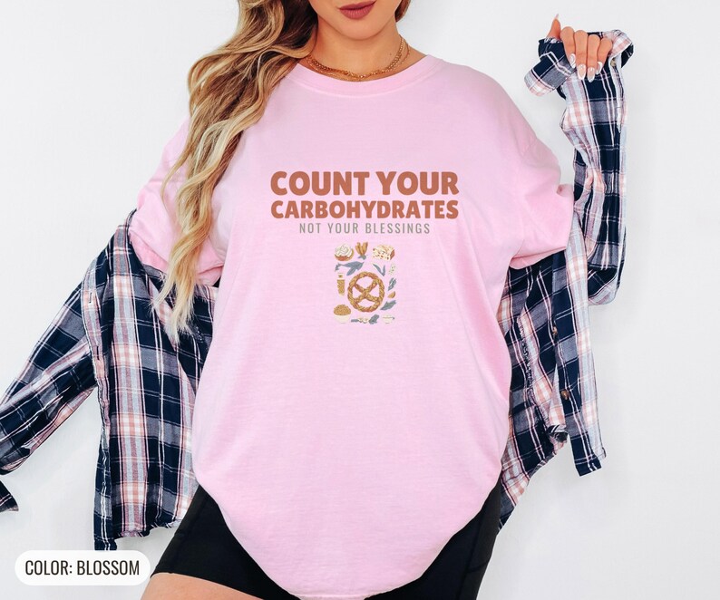 Blossom Comfort Colors t-shirt printed with the words Count Your Carbohydrates Not Your Blessings and a drawing of a golden-brown braided pretzel with coarse salt grains, worn by a woman