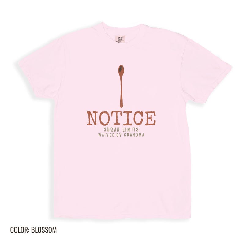 Blossom Comfort Colors t-shirt printed with the words Notice Sugar Limits Waived By Grandma and a drawing of a painted wooden spoon crossed over a cinnamon stick bundle, folded flat lay