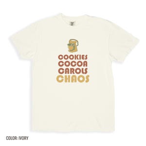 Ivory Comfort Colors t-shirt printed with the words Cookies Cocoa Carols Chaos and a drawing of a retro metal hand mixer with steel beaters, folded flat lay