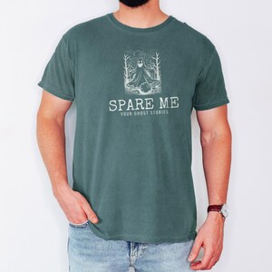 Blue Spruce Comfort Colors t-shirt printed with the words Spare Me Your Ghost Stories and a drawing of a friendly sheet ghost rolling a bowling ball towards a set of bowling pins, worn by a man