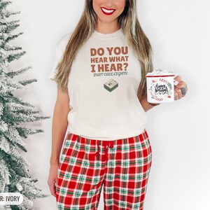 Ivory Comfort Colors t-shirt printed with the words Do You Hear What I Hear? Just Call Lights and a drawing of a rectangular electronic medical pager with a small holly sprig beside it, worn by a woman